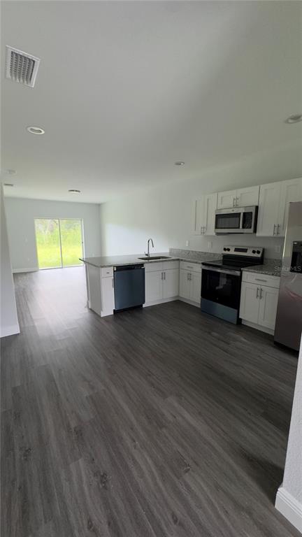 A modern kitchen features white cabinets, stainless steel appliances, and gray wood-look flooring — 2217 FRASER STREET, PORT CHARLOTTE, FL