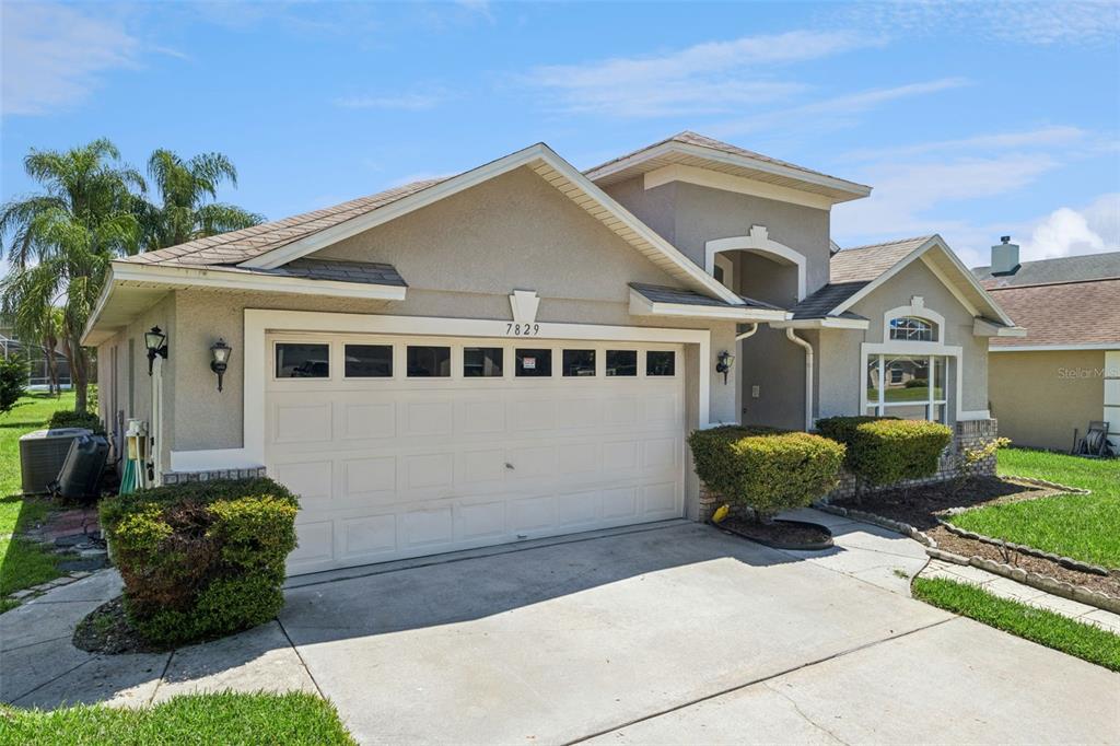 A single-story house with a beige stucco exterior, a two-car garage, and a front lawn — 7829 ELMSTONE CIRCLE, ORLANDO, FL