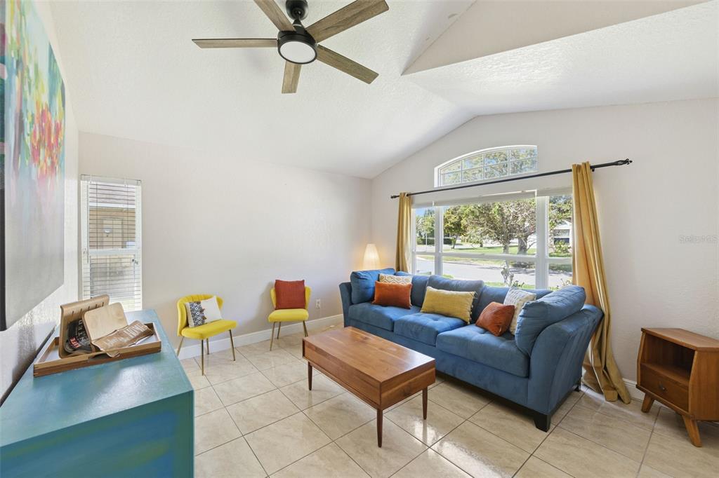 A living room features a blue sofa, wooden coffee table, yellow chairs, and tile flooring — 7829 ELMSTONE CIRCLE, ORLANDO, FL