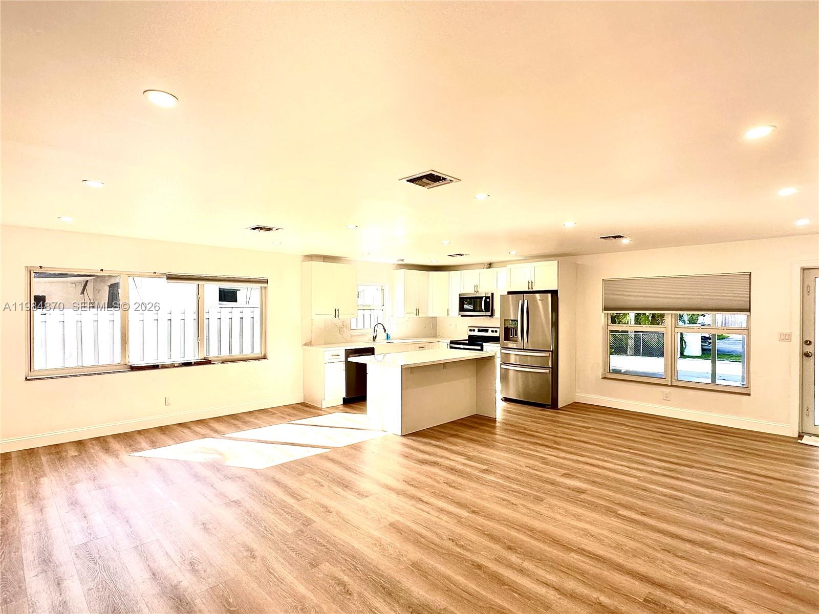 An open-concept kitchen features white cabinetry, a center island, and wood-look flooring — 3042 Hayes St, Hollywood FL 33021, HOLLYWOOD, FL