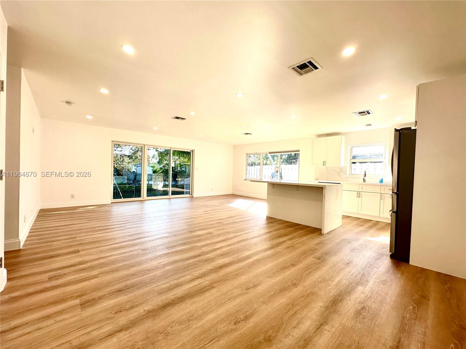 An open-concept kitchen and living area features light wood-look flooring and white cabinetry — 3042 Hayes St, Hollywood FL 33021, HOLLYWOOD, FL