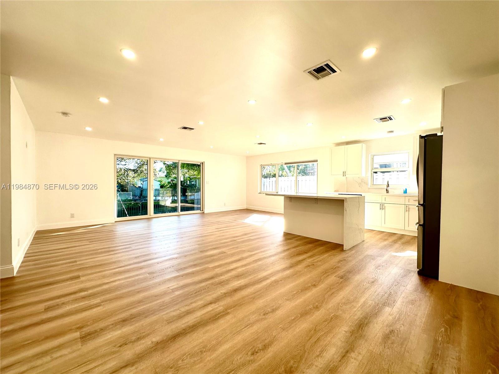 An open-concept kitchen and living area features light wood flooring and white cabinetry — 3042 Hayes St, Hollywood FL 33021, HOLLYWOOD, FL
