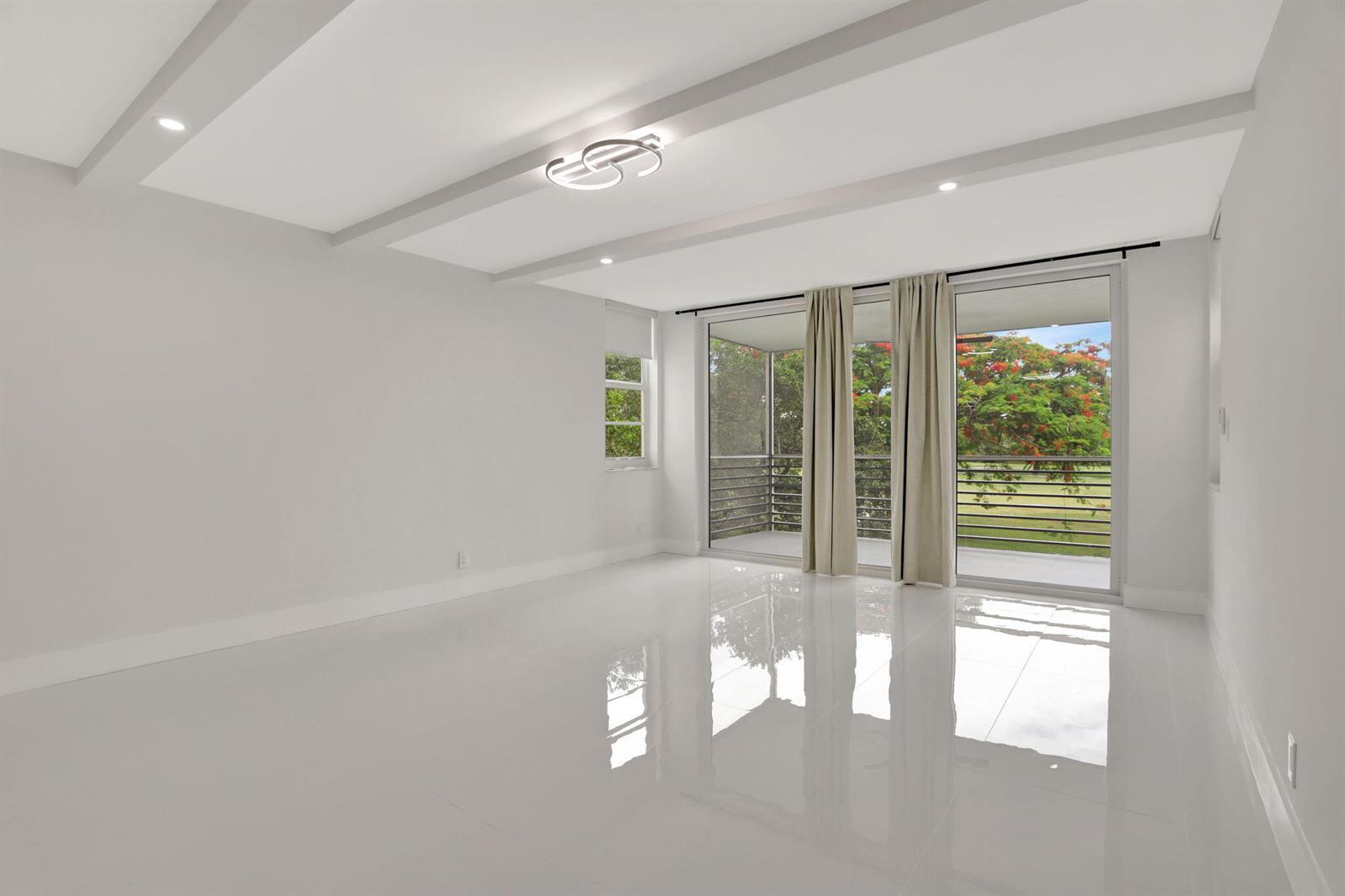 A bright, empty room features white tile floors, a coffered ceiling, and sliding glass doors — 3505 Oaks Way # 204, Pompano Beach FL 33069, POMPANO BEACH, FL