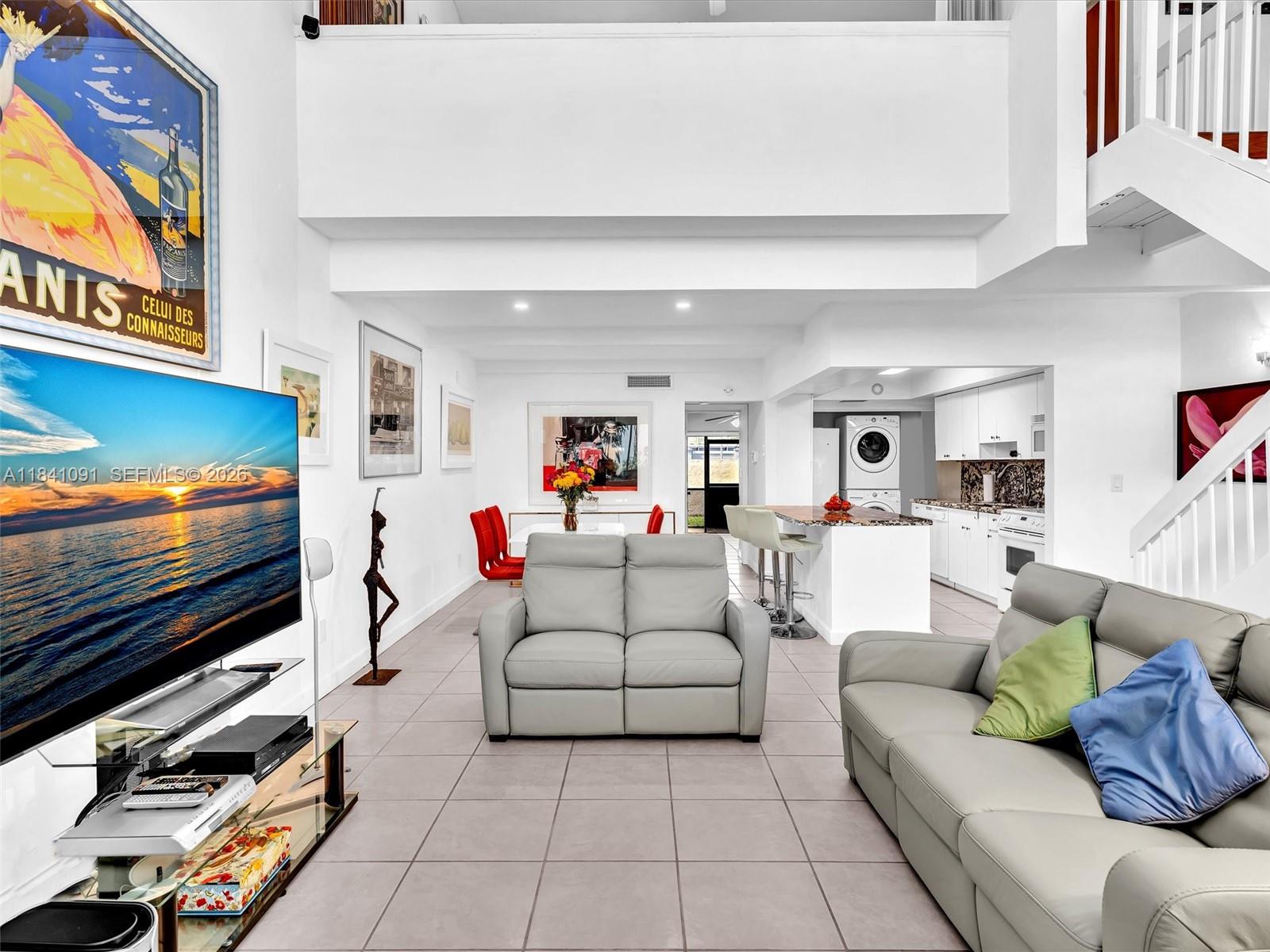 A bright, open-concept living room and kitchen area with light tile flooring and white walls — 19200 NE 25th Ave # 323C, Miami FL 33180, MIAMI, FL