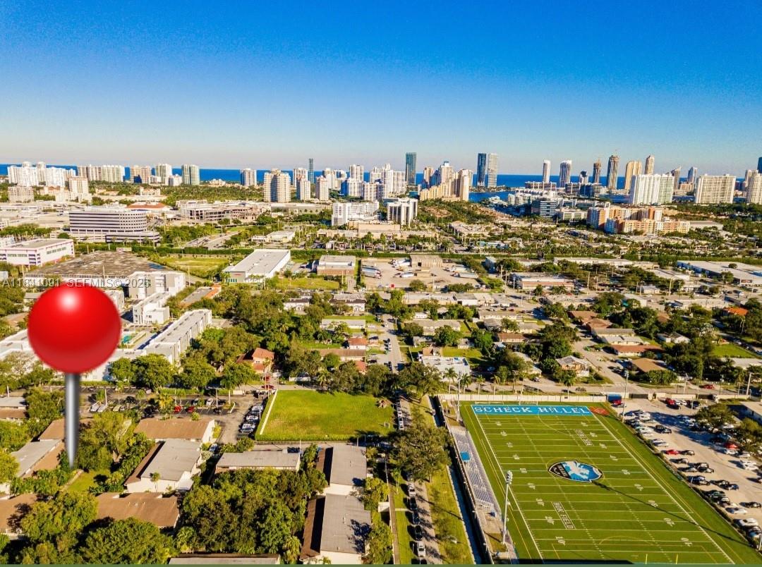 An aerial view shows a residential area with a football field and a distant city skyline — 19200 NE 25th Ave # 323C, Miami FL 33180, MIAMI, FL