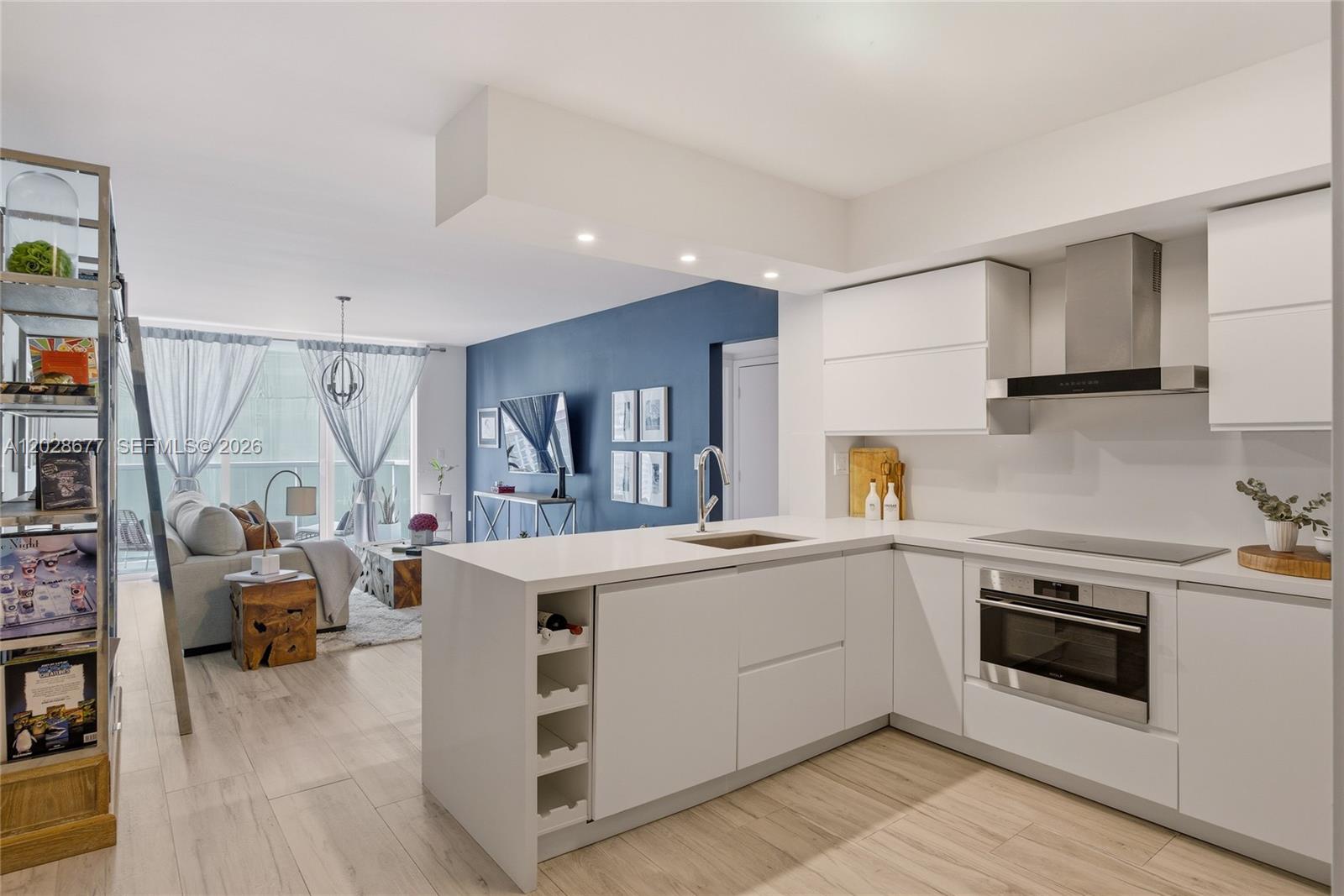 A modern open-concept kitchen with white cabinetry and a peninsula overlooks a living room area — 31 SE 5th St # 2410, Miami FL 33131, MIAMI, FL
