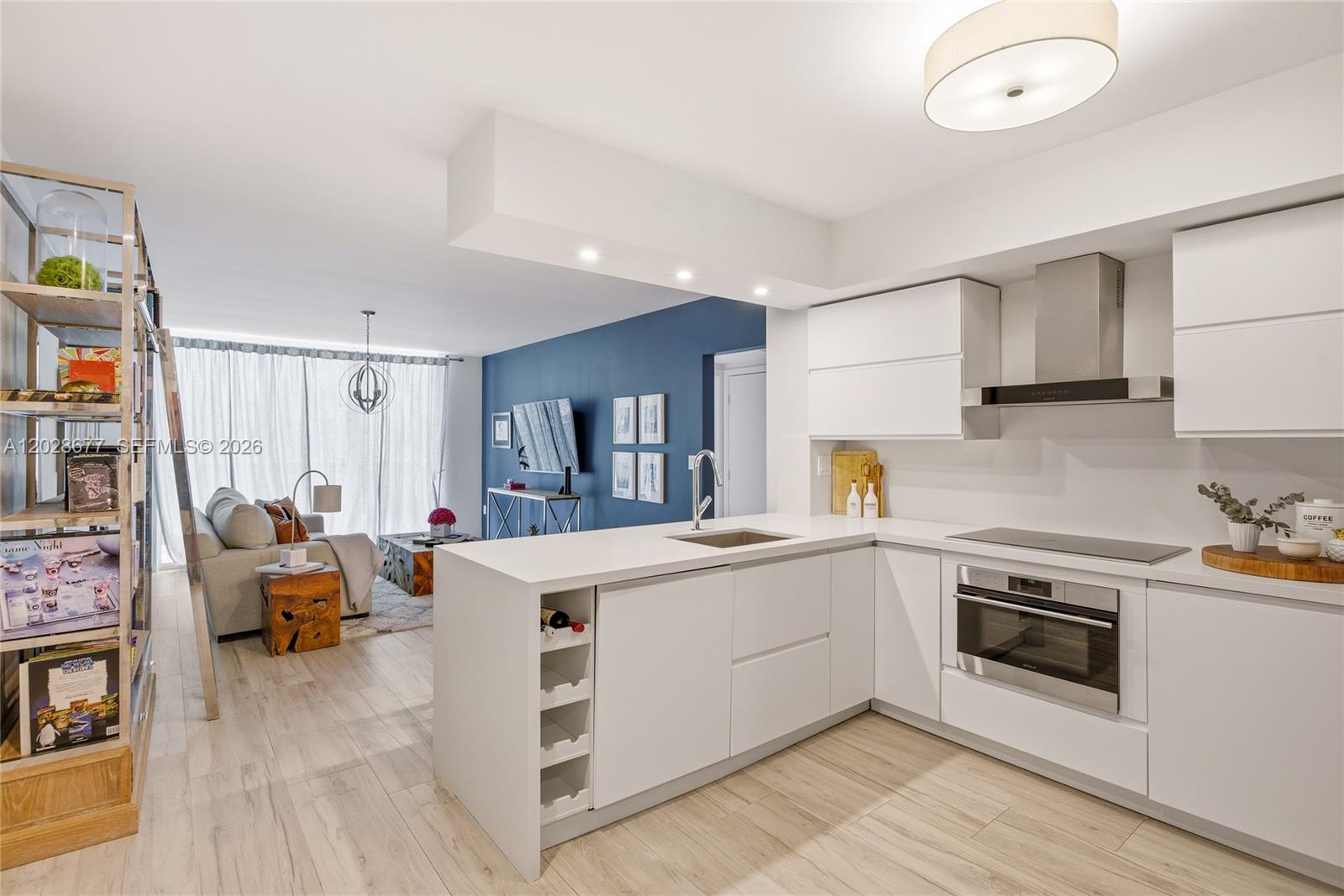 A modern kitchen with white cabinetry and a peninsula overlooks a living area with blue walls — 31 SE 5th St # 2410, Miami FL 33131, MIAMI, FL