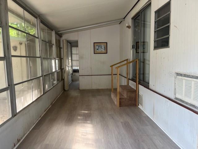 An enclosed porch features light wood-look flooring, white paneled walls, large windows, and small carpeted steps — 3000 CLARCONA ROAD UNIT 438, APOPKA, FL