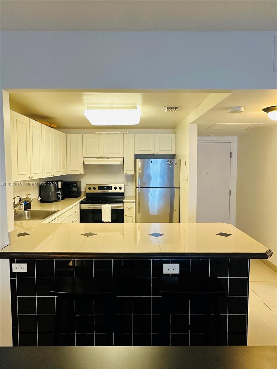 A kitchen features white cabinets, stainless steel appliances, and a black-tiled breakfast bar — 2301 Collins Ave # 420, Miami Beach FL 33139, MIAMI BEACH, FL