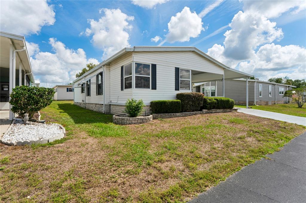 A white manufactured home features a carport, a small front lawn, and stone skirting — 37621 ROSALITA AVENUE, ZEPHYRHILLS, FL