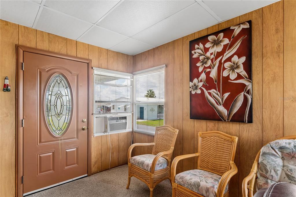 A sunroom features wood-paneled walls, a brown front door, two wicker chairs, and a window unit — 37621 ROSALITA AVENUE, ZEPHYRHILLS, FL