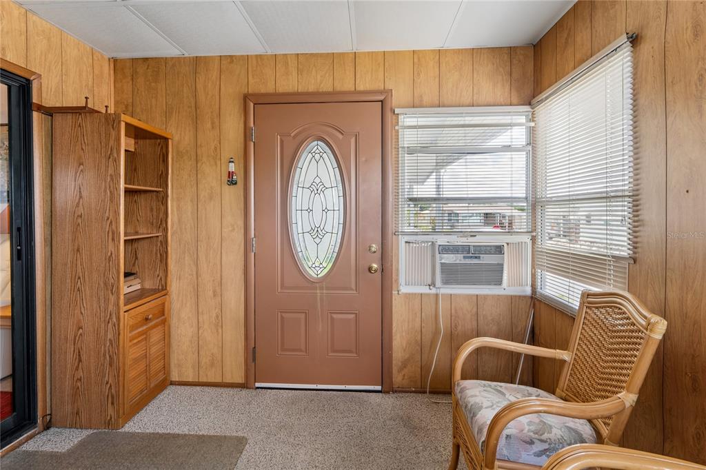 A sunroom features wood-paneled walls, a brown front door, a window air conditioner, and wicker chairs — 37621 ROSALITA AVENUE, ZEPHYRHILLS, FL