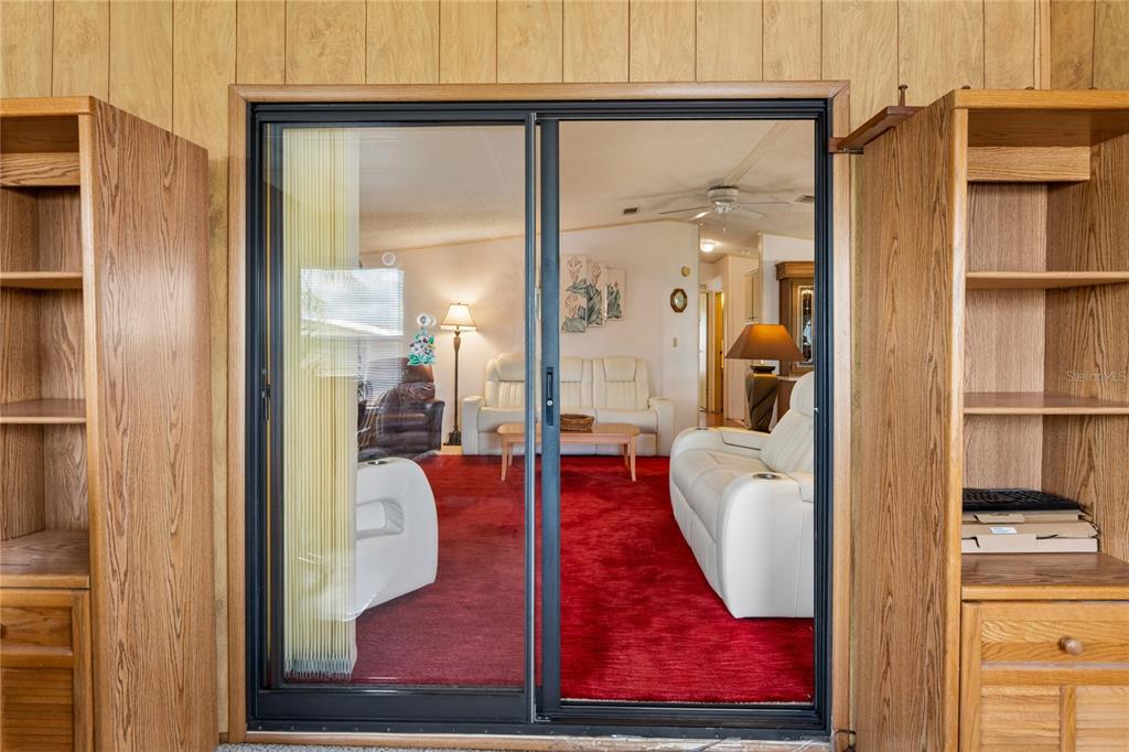 A sliding glass door opens into a living room featuring red carpeting and white furniture — 37621 ROSALITA AVENUE, ZEPHYRHILLS, FL