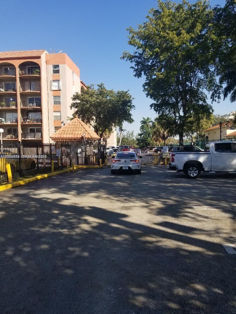 A white car approaches a gated entrance next to a multi-story apartment building — 5201 NW 7th St # 408, Miami FL 33126, MIAMI, FL