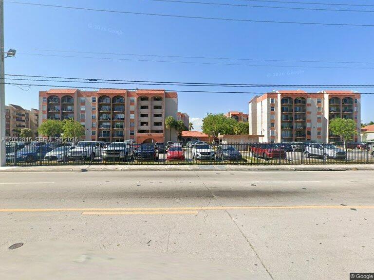 A street-level view of two multi-story apartment buildings behind a metal fence and parking lot — 5201 NW 7th St # 408, Miami FL 33126, MIAMI, FL