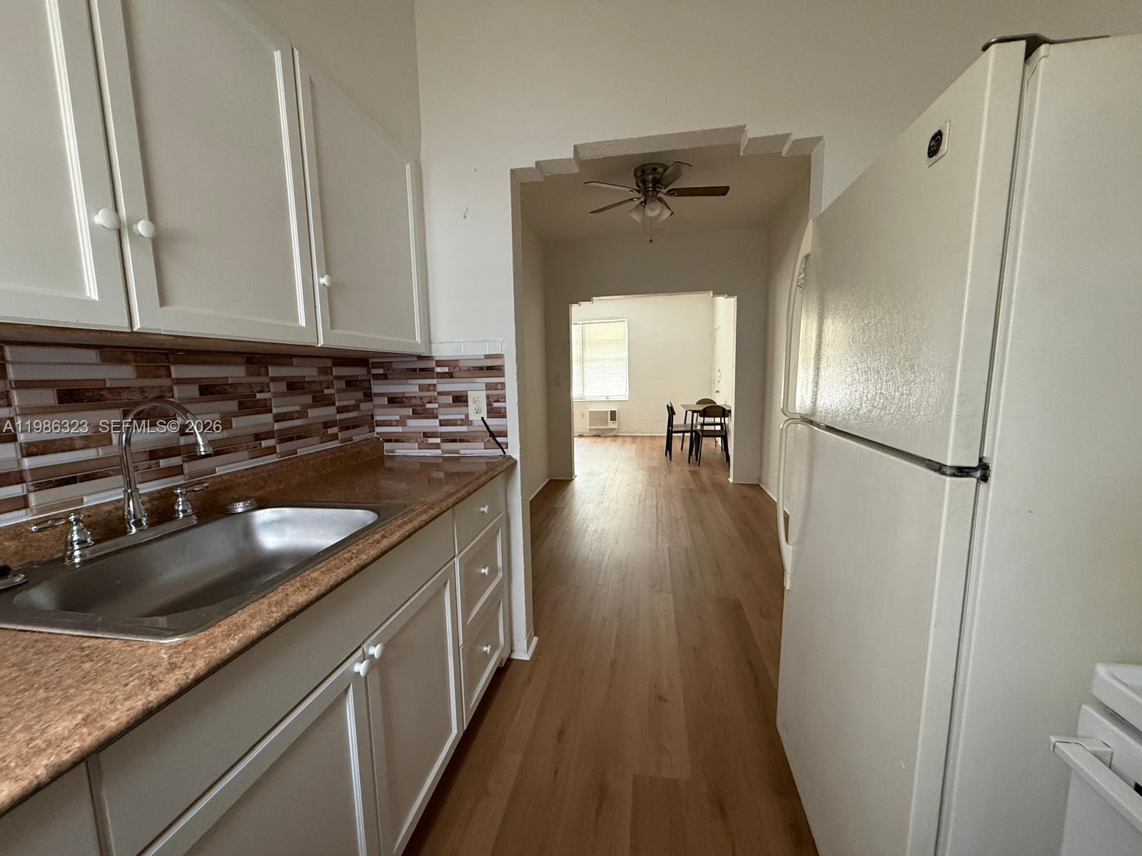 A kitchen with white cabinets and a brown countertop opens into a dining area — 6830 Harding Ave # 1, Miami Beach FL 33141, MIAMI BEACH, FL