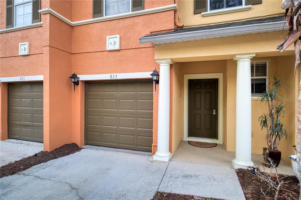 The exterior of a two-story townhouse features a garage, a covered entryway, and stucco walls — 873 ASSEMBLY COURT, REUNION, FL