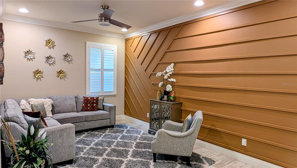 A living room features a gray sectional sofa, a patterned rug, and a geometric accent wall — 2468 WHITTLER BRANCH, ODESSA, FL