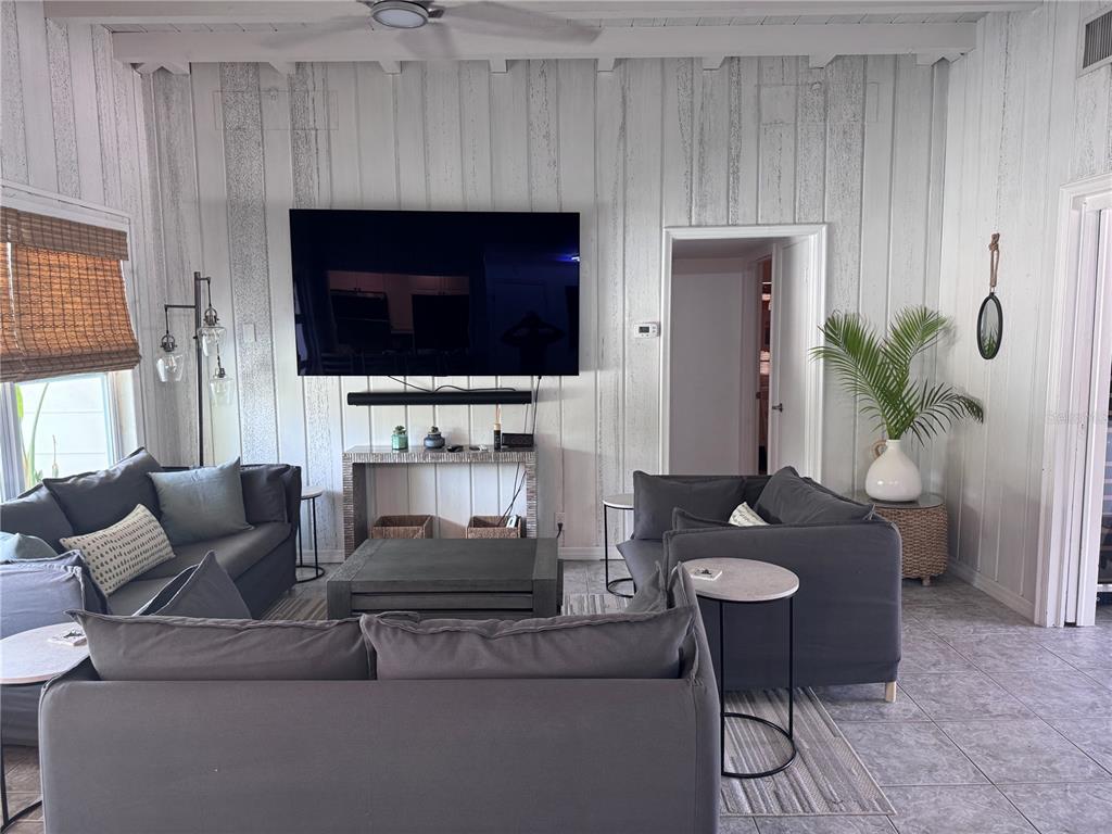 A living room features gray sofas, a wall-mounted television, and white vertical wood paneling — 6304 BEECHWOOD AVENUE, SARASOTA, FL