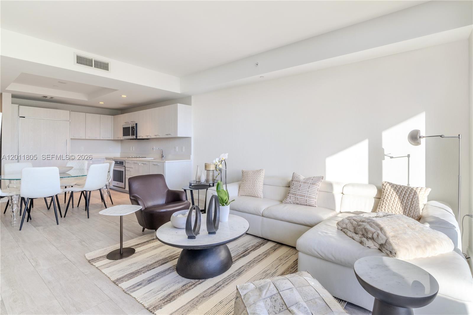 A modern open-concept living room and kitchen feature white cabinetry, light flooring, and neutral furniture — 55 SW 9th St # 3404, Miami FL 33130, MIAMI, FL