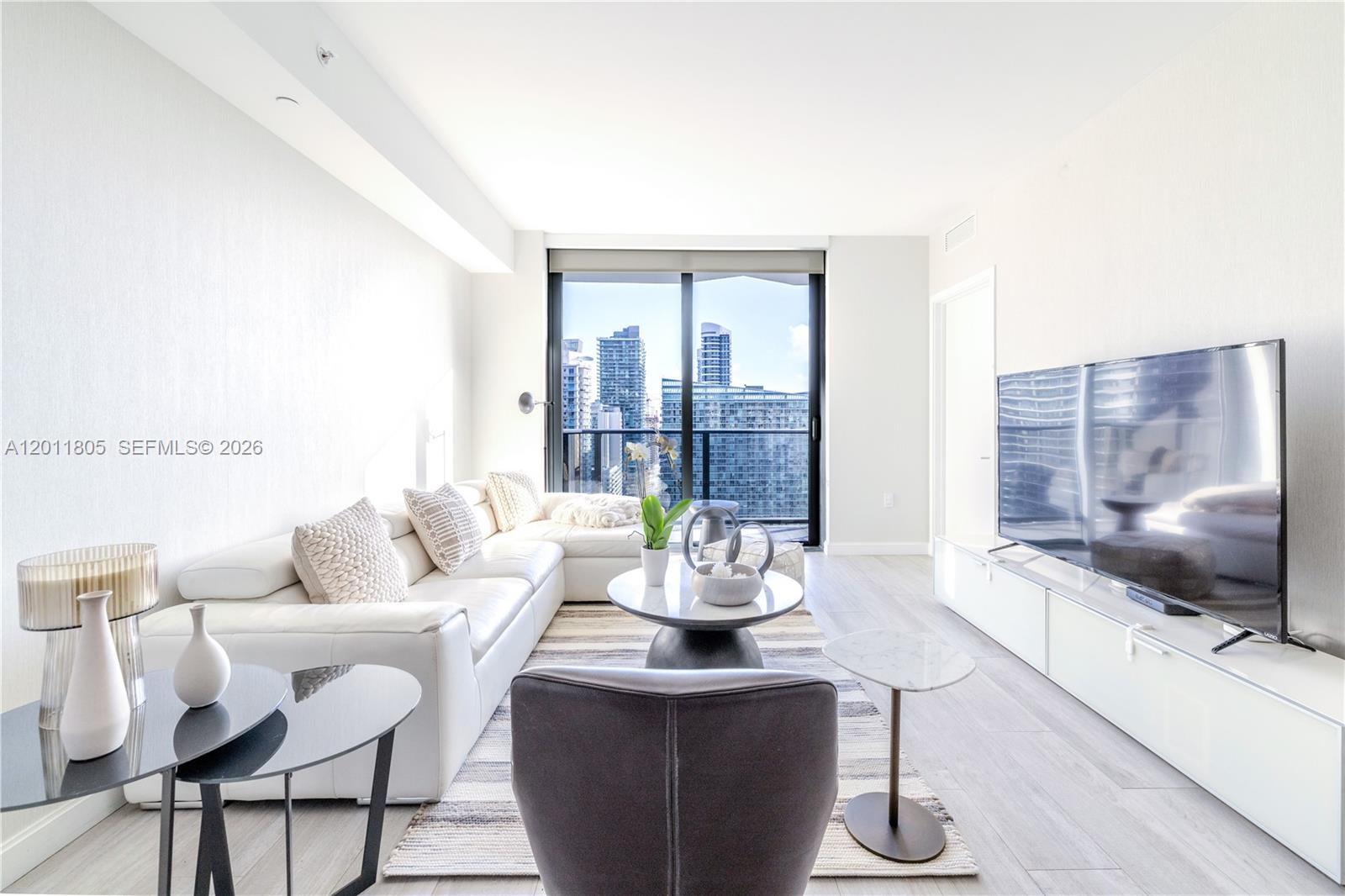 A modern living room features a white sectional sofa, a television, and floor-to-ceiling windows — 55 SW 9th St # 3404, Miami FL 33130, MIAMI, FL