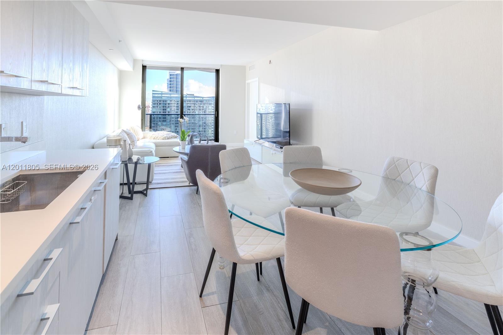 A modern open-concept living and dining area features a kitchen, glass table, and balcony view — 55 SW 9th St # 3404, Miami FL 33130, MIAMI, FL