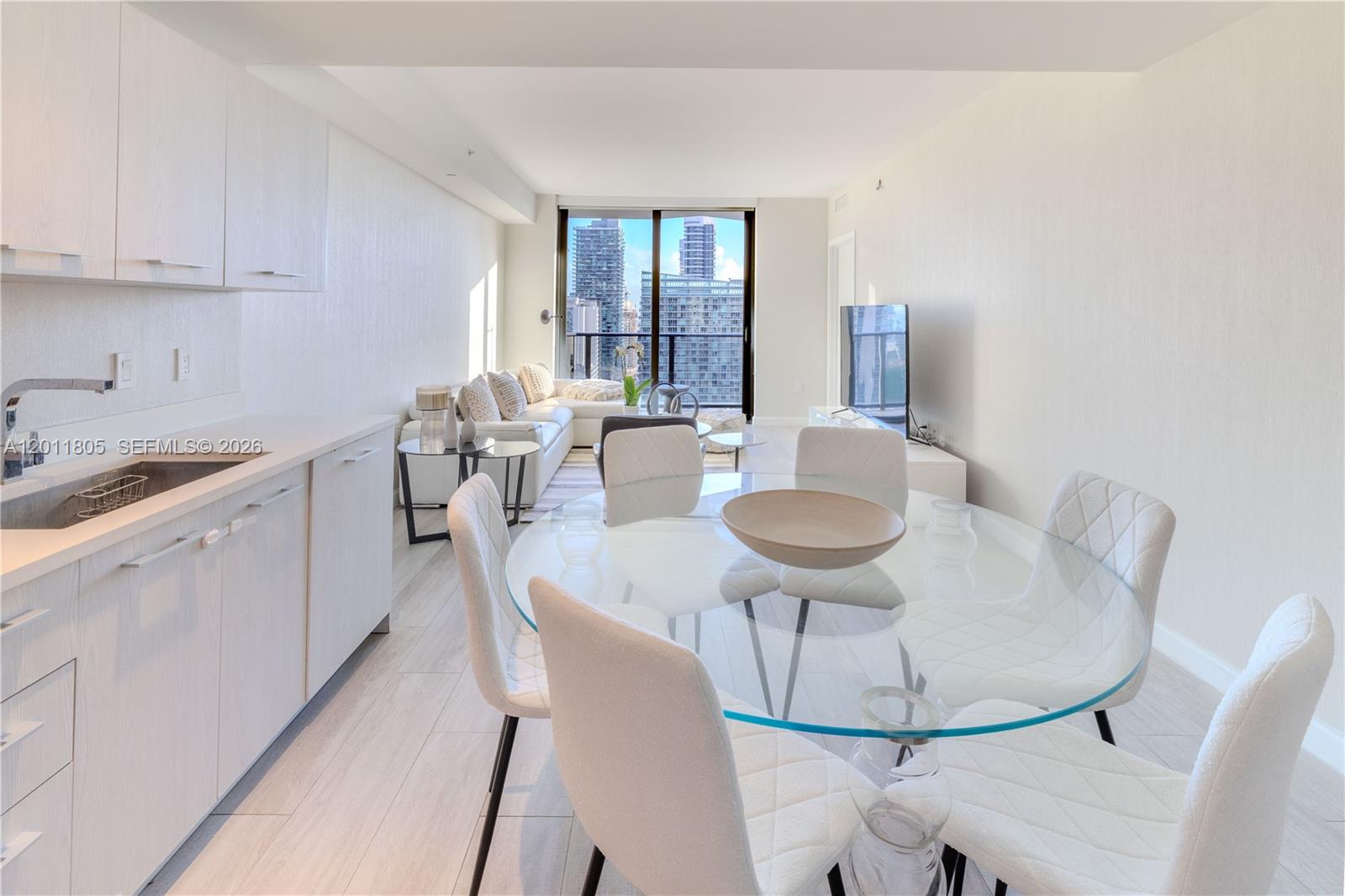 A modern open-plan living and dining area features white cabinetry, a glass table, and city views — 55 SW 9th St # 3404, Miami FL 33130, MIAMI, FL