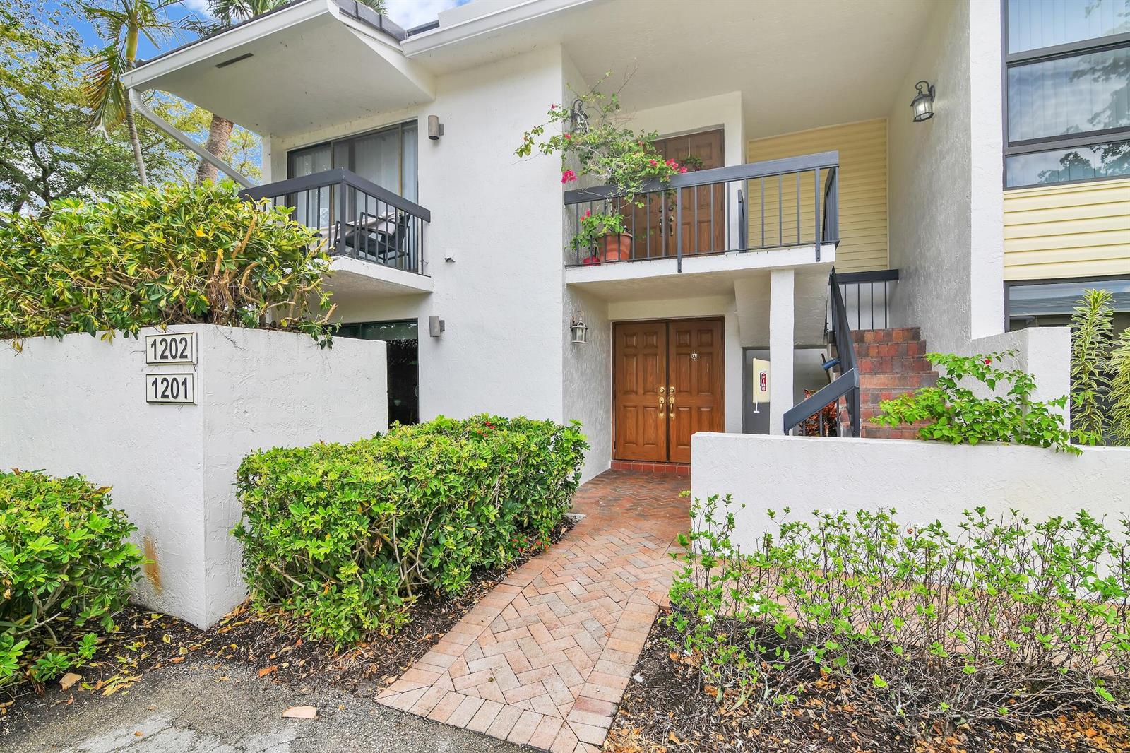 A two-story building exterior features a brick walkway leading to a double wooden front door — 6760 Willow Wood Drive # 1201, Boca Raton FL 33434, BOCA RATON, FL