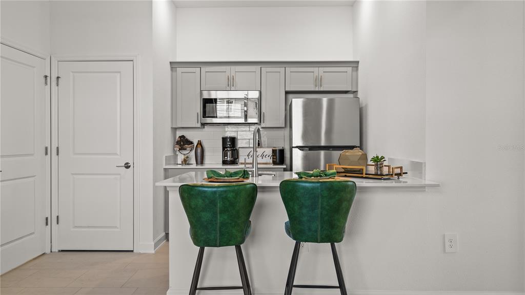 A kitchen features gray cabinets, stainless steel appliances, a white countertop, and two green stools — 4014 EASTMINSTER ROAD, DAVENPORT, FL