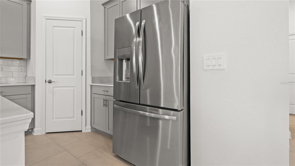A stainless steel refrigerator stands in a kitchen with gray cabinets and white walls — 4014 EASTMINSTER ROAD, DAVENPORT, FL