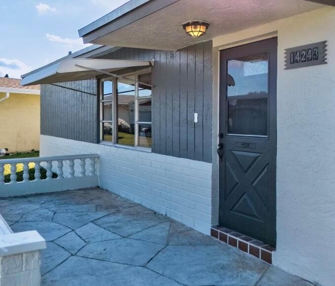 A gray front door and vertical siding contrast with a white brick wall and patio — 14243 EL CLAVEL Way, Delray Beach FL 33484, DELRAY BEACH, FL