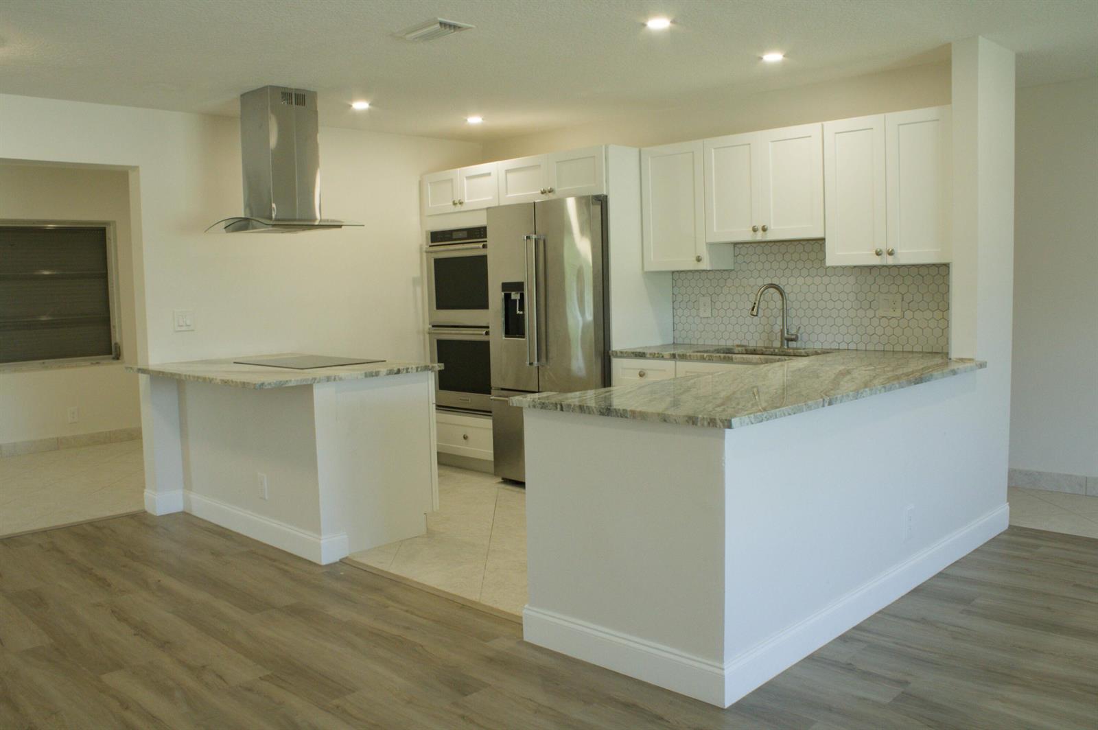 A kitchen with white cabinets, stainless steel appliances, and granite countertops features a peninsula island — 14243 EL CLAVEL Way, Delray Beach FL 33484, DELRAY BEACH, FL