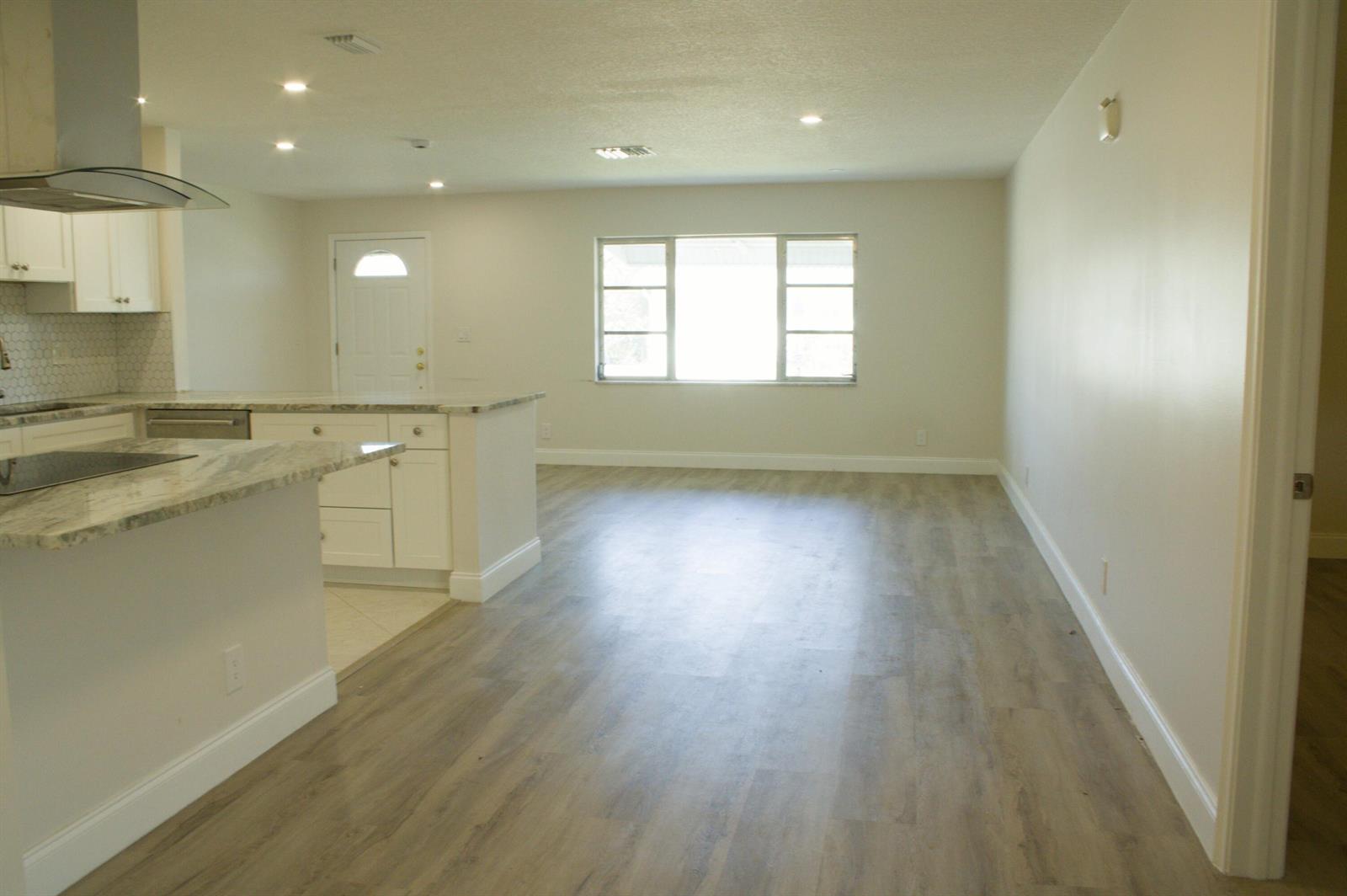 A kitchen with white cabinets and stone countertops opens into a living area with wood-look flooring — 14243 EL CLAVEL Way, Delray Beach FL 33484, DELRAY BEACH, FL