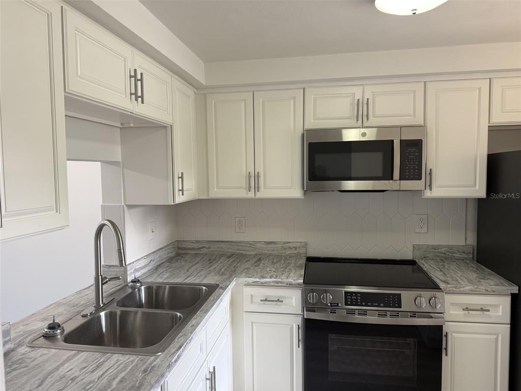 A kitchen featuring white cabinets, a stainless steel microwave, and a grey marble-patterned countertop — 4413 SUNSTATE DRIVE UNIT 0, NEW PORT RICHEY, FL