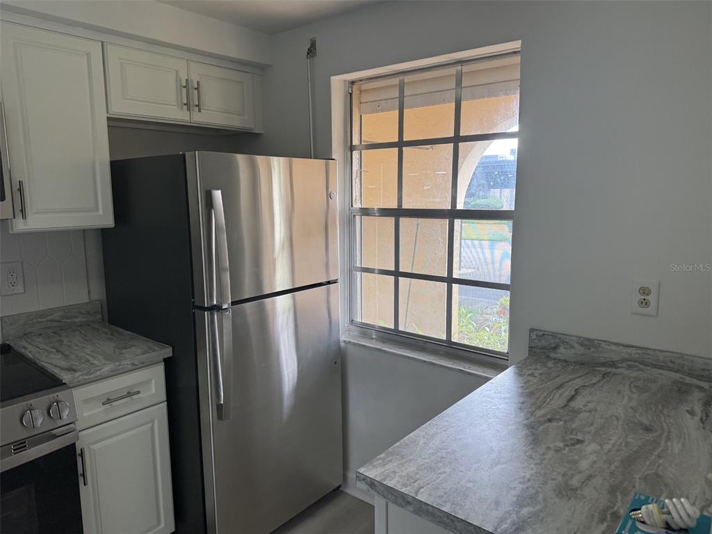A kitchen features a stainless steel refrigerator, white cabinets, and gray marble-patterned countertops — 4413 SUNSTATE DRIVE UNIT 0, NEW PORT RICHEY, FL