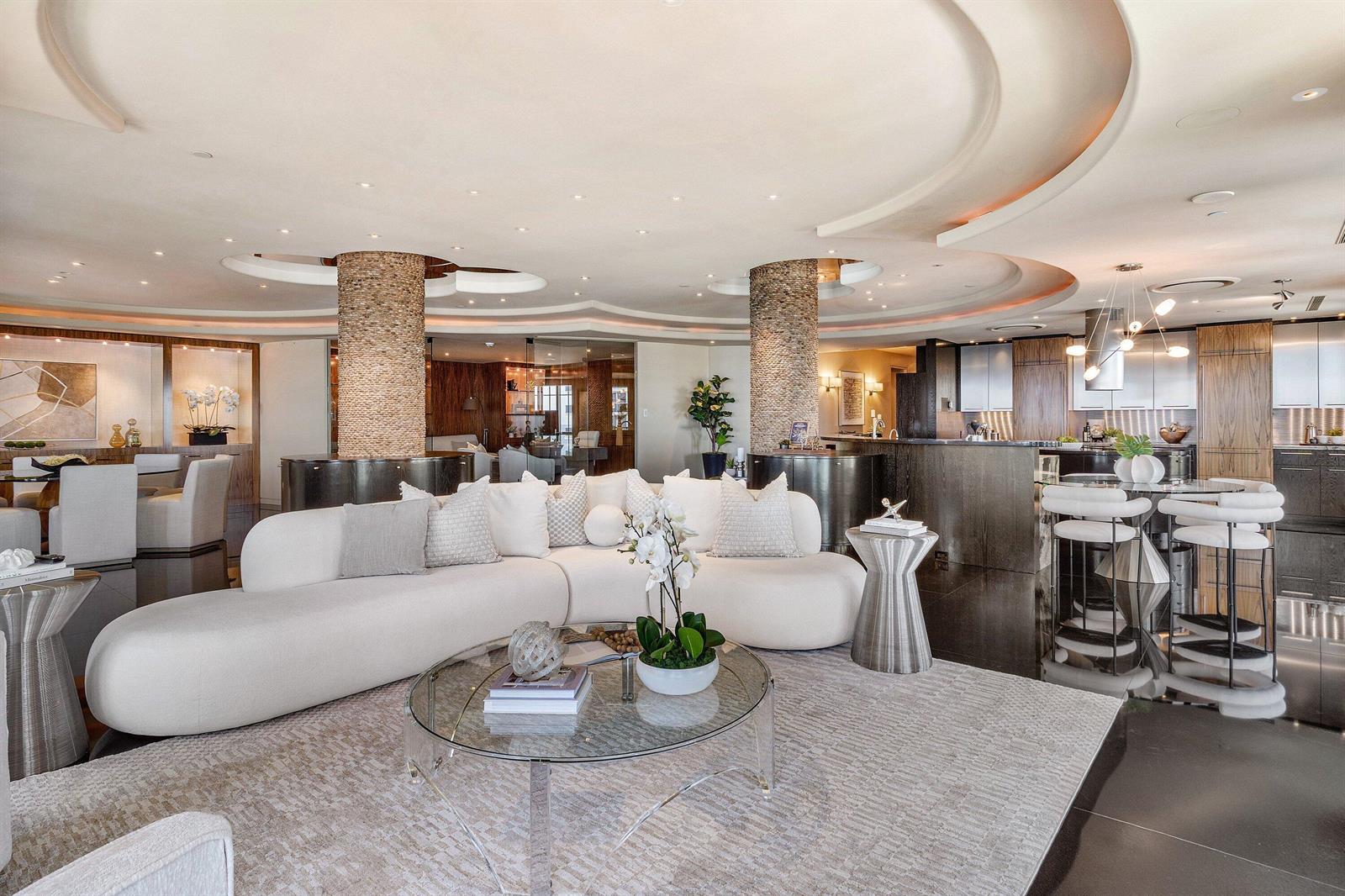 A modern open-concept living room features a curved white sofa, stone columns, and dark flooring — 400 S Ocean Boulevard, Boca Raton FL 33432, BOCA RATON, FL
