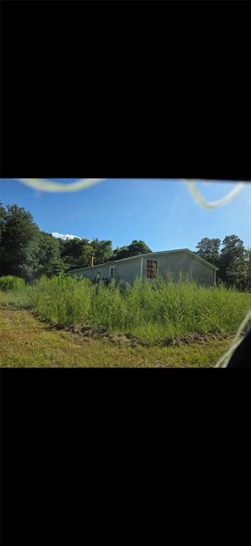 A single-story house with light-colored siding sits in a field of tall, overgrown grass — 210 SANTA ROSA ROAD, CANTONMENT, FL