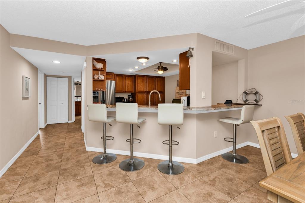 A kitchen with wood cabinets and a breakfast bar featuring four white stools — 9050 MIDNIGHT PASS ROAD UNIT 1, SARASOTA, FL