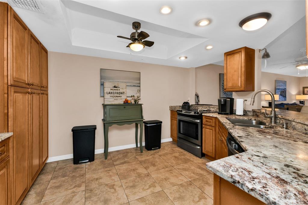 A kitchen features wood cabinets, granite countertops, stainless steel appliances, and a tiled floor — 9050 MIDNIGHT PASS ROAD UNIT 1, SARASOTA, FL