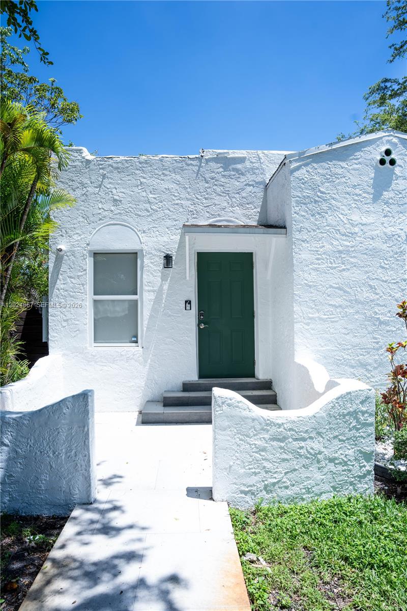 A white stucco house features a green front door, arched window, and low courtyard walls — 247 NW 58th St, Miami FL 33127, MIAMI, FL