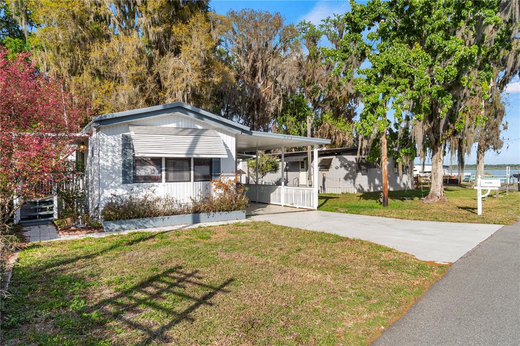 A white mobile home with a carport and a front yard sits under large trees — 942 CR 461, LAKE PANASOFFKEE, FL