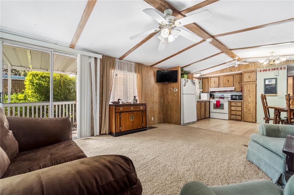 A living room with wood-paneled walls, carpeted floors, and an open kitchen in the background — 942 CR 461, LAKE PANASOFFKEE, FL