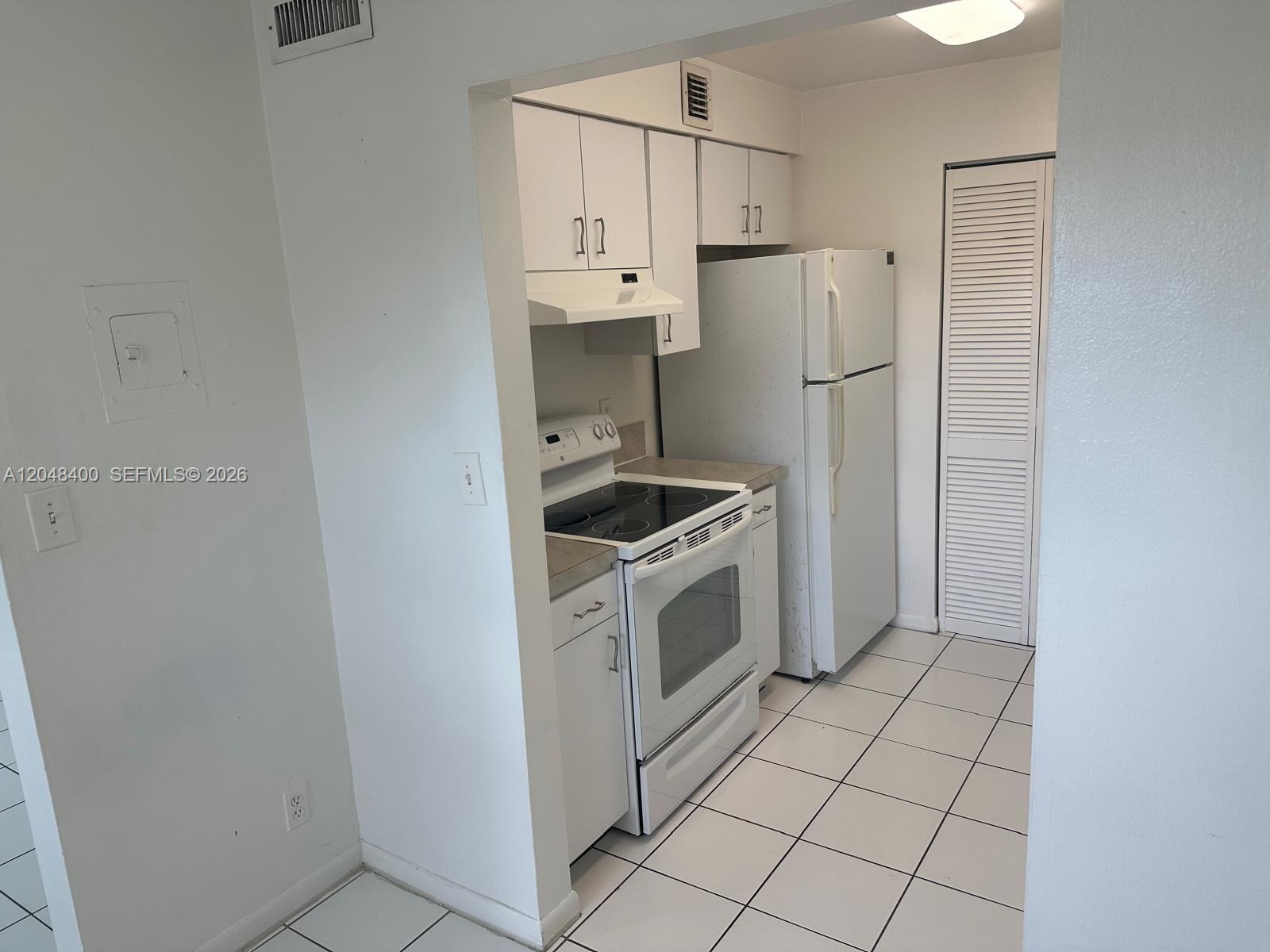 A small kitchen features white cabinets, a white electric stove, and white tile flooring — 500 NE 2nd St # 408, Dania Beach FL 33004, DANIA BEACH, FL