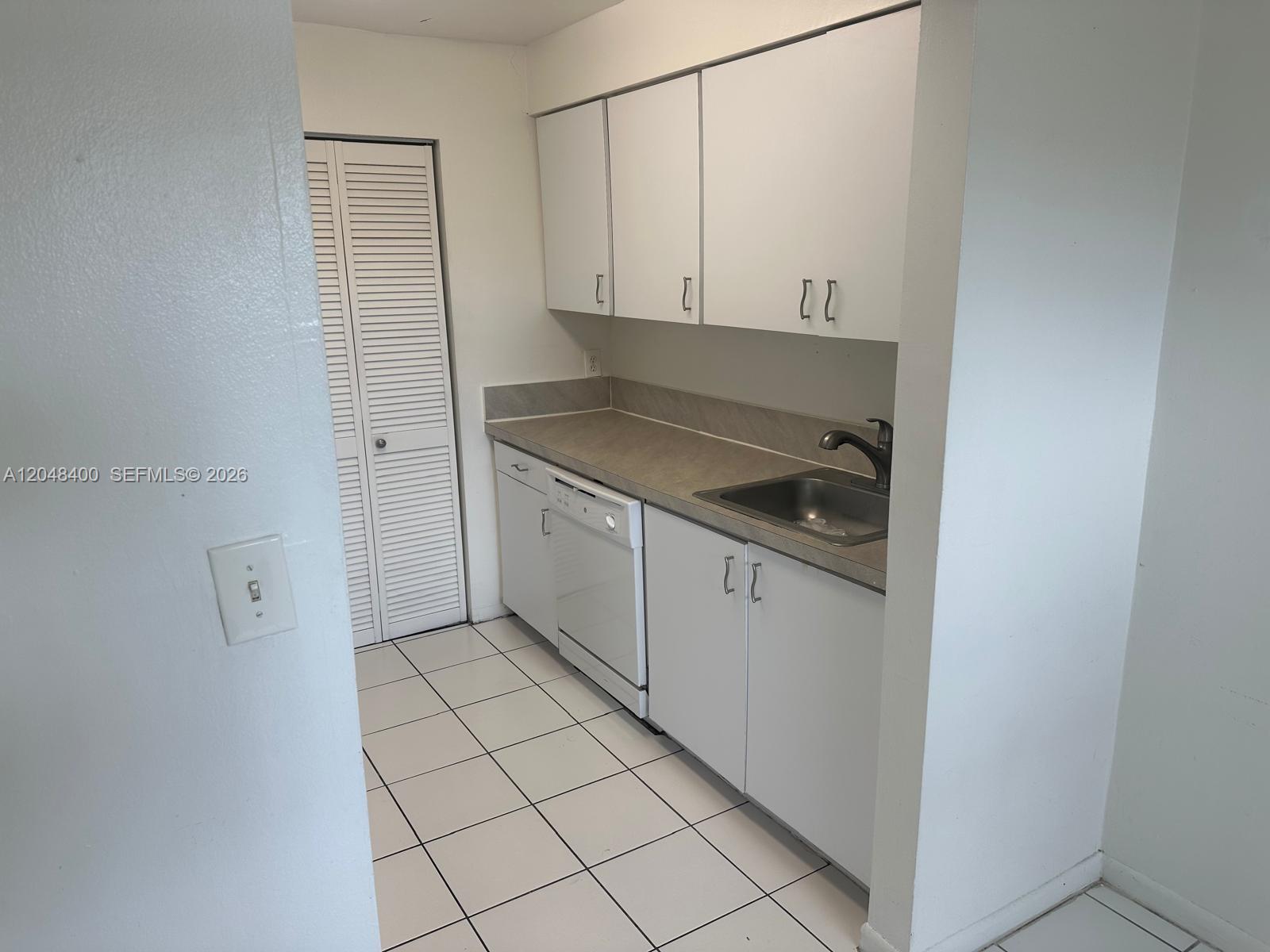 A small kitchen features white cabinets, a dishwasher, a stainless steel sink, and tiled flooring — 500 NE 2nd St # 408, Dania Beach FL 33004, DANIA BEACH, FL