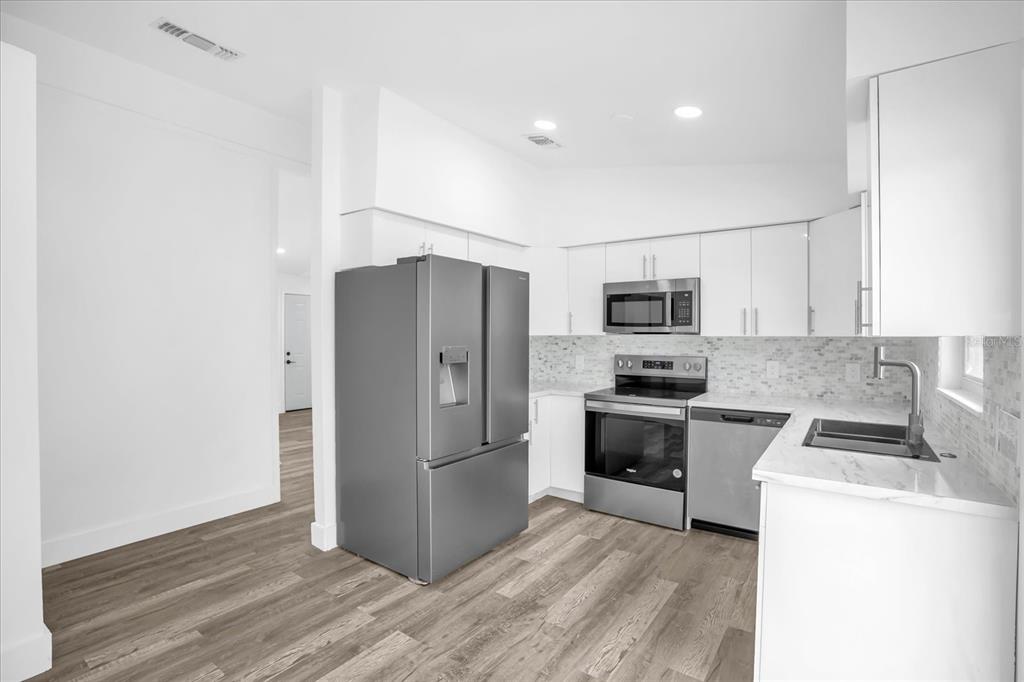 A modern kitchen features white cabinets, stainless steel appliances, and wood-look flooring — 1730 AVENUE C NE, WINTER HAVEN, FL