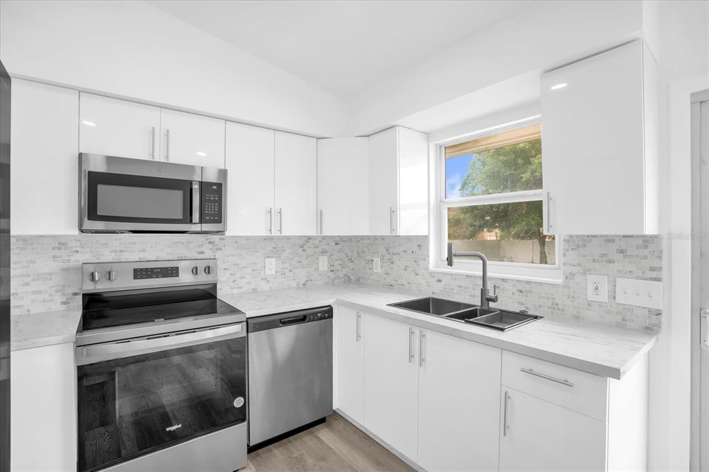 A modern kitchen features white cabinets, stainless steel appliances, and a light-colored tiled backsplash — 1730 AVENUE C NE, WINTER HAVEN, FL