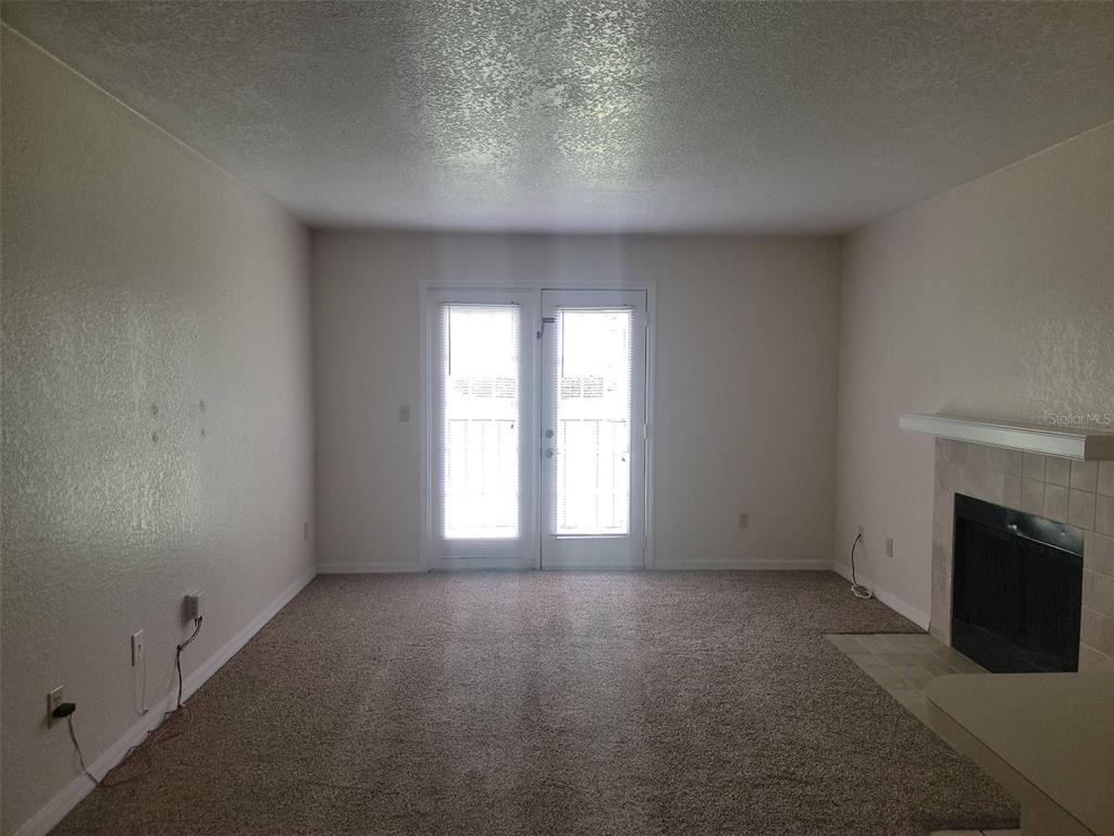 A living room features beige carpet, light-colored walls, a fireplace, and glass double doors — 2550 N ALAFAYA TRAIL UNIT 5105, ORLANDO, FL
