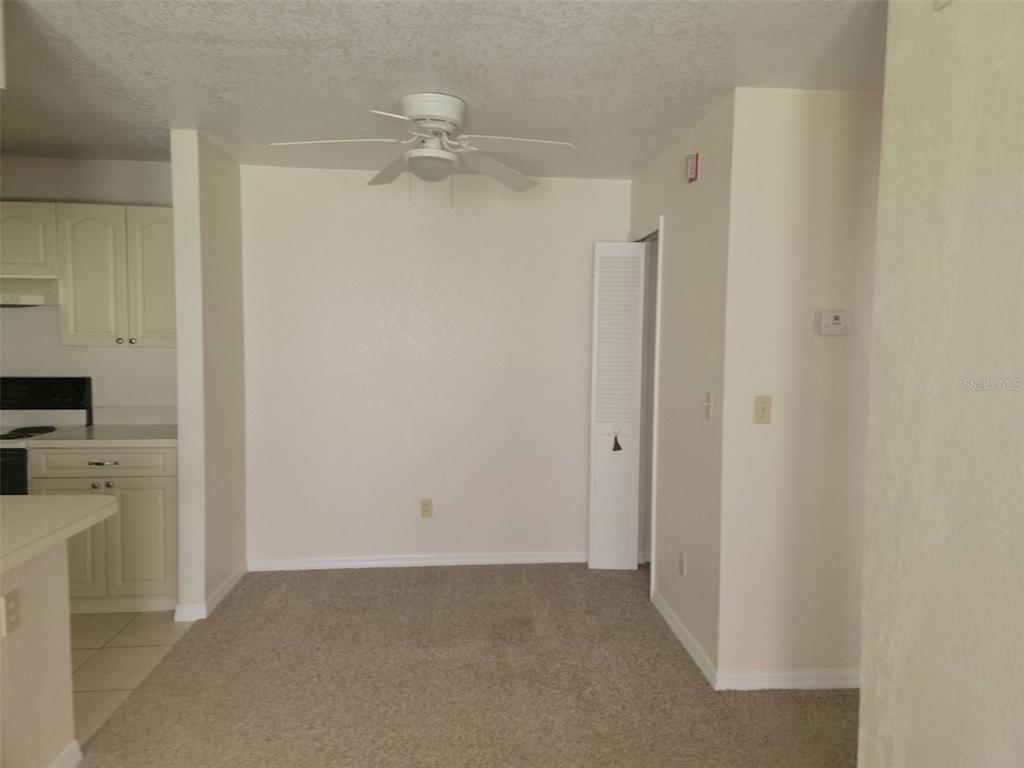 An empty dining area features beige carpet, a ceiling fan, and an adjacent kitchen — 2550 N ALAFAYA TRAIL UNIT 5105, ORLANDO, FL