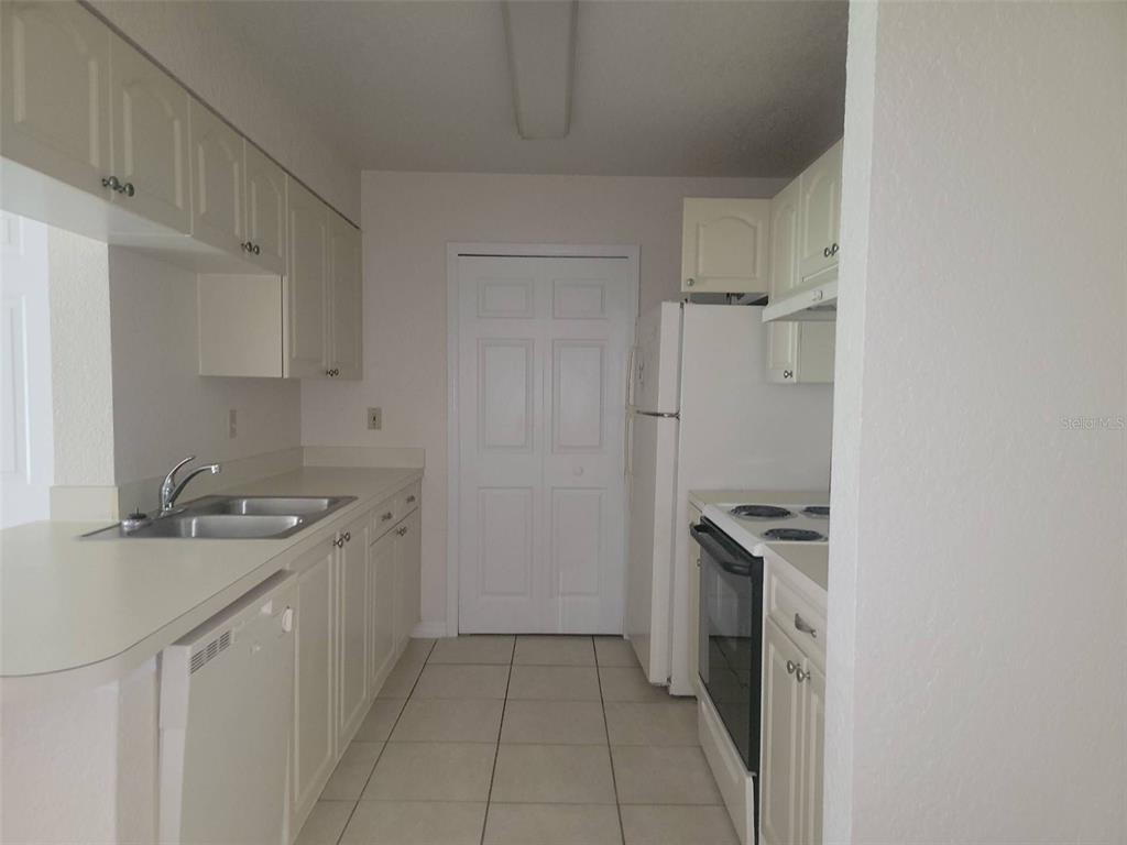 A galley-style kitchen features white cabinets, white appliances, and light-colored tile flooring — 2550 N ALAFAYA TRAIL UNIT 5105, ORLANDO, FL