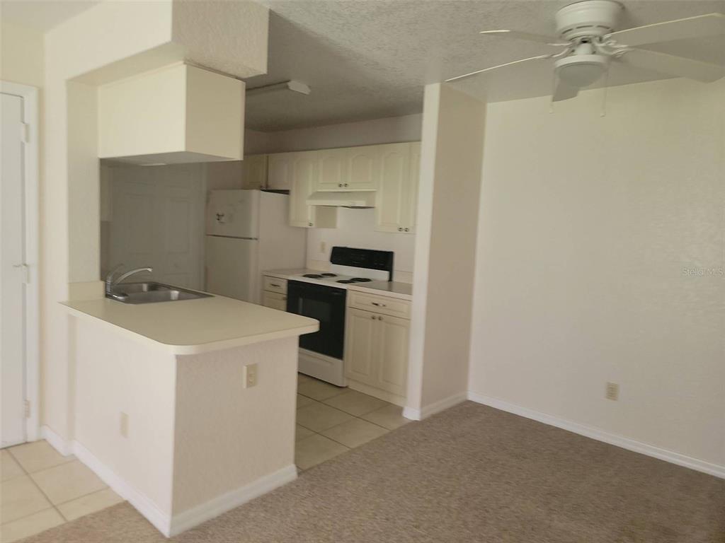 A kitchen with white cabinets and appliances overlooks a carpeted dining area with a ceiling fan — 2550 N ALAFAYA TRAIL UNIT 5105, ORLANDO, FL